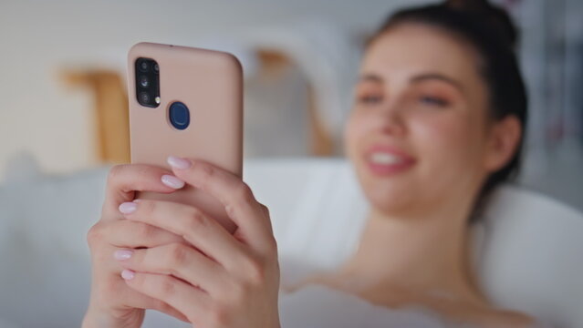 Brunette messaging cellphone bathing in home bathroom closeup. Smiling woman
