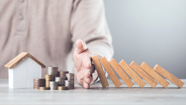 Businessman uses his hand to stop wooden blocks from falling, symbolizing the protection of assets and strategic decision-making in managing resources effectively, domino effect and risk management