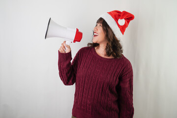 Excited young asian woman wearing santa clause hat and red long sleeved sweater is using megaphone with smiling face expression, isolated on white background. Concept for Christmas and New Year Party