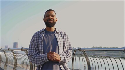 Positive attractive cool bearded African American man blogger live streaming vlog, communicating and sharing with online audience while walking on city street on sunny summer day