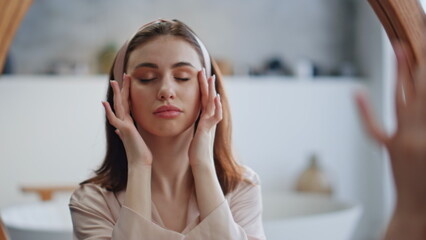 Relaxed girl massaging facial skin in bathroom mirror closeup. Closed eyes woman