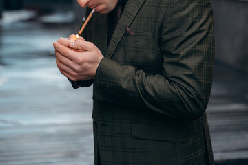 An adult man in a businessman's jacket smokes a cigarette on a dark background. Smoke and bad habits