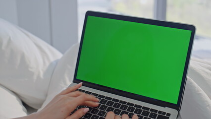 Freelancer typing green screen laptop in bed morning home closeup. Woman hands