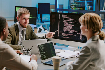 Group of three young data security specialists discussing ways of upgrading computer systems during...