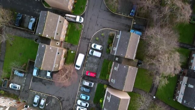 Top-Down view of a residential area in Edinburgh, featuring buildings, parking lots, and roadways. Cars are visible on streets and driveways, with green spaces and trees between housing units.