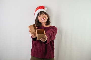 Excited young asian woman wearing santa clause hat and red long sleeved sweater is opening small gift box, isolated over white background. Concept for Christmas Holiday and New Year Party.