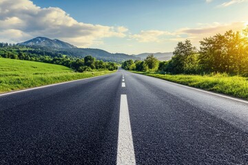 A long, straight asphalt road with a white dividing line in the center, leading through a green valley towards distant mountains and a bright blue sky with puffy clouds.