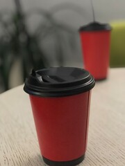 Red Takeaway Coffee Cup with Black Lid on Table - Close-Up, Highlighting Depth of Field and Focus on Foreground Cup Against Blurred Background