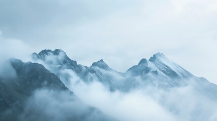Obraz premium The snow-capped mountains rise above the clouds, creating a stunning scene. The peaks are shrouded in mist, adding to the sense of mystery and wonder.