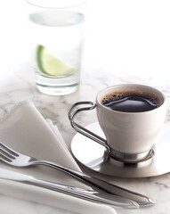 Café em xícara sofisticada em mesa de mármore com copo de água com limão ao fundo