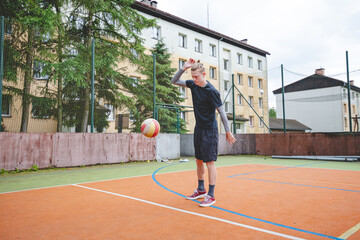Fototapeta premium Volleyball player standing on a hard court, bouncing the ball while preparing for the next play during an outdoor game. A calm, focused moment before the action begins