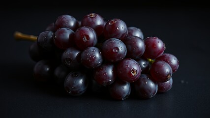 Fototapeta premium A cluster of dark red grapes glistening with water droplets, set against a stark black background, highlighting the subtle textures and hues of the fruit.