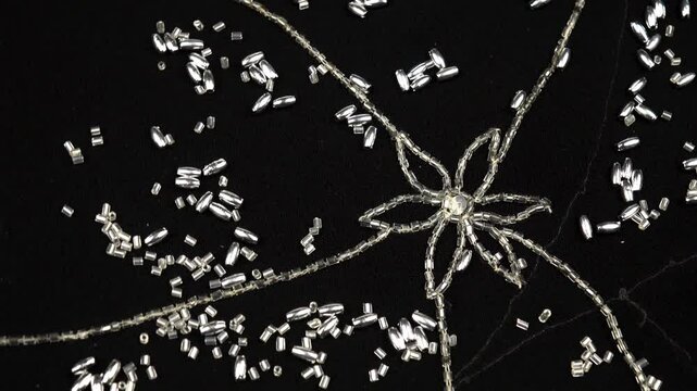 Silver beads are scattered on black chiffon with bead embroidery. Handicrafts and sewing, background