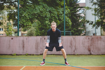 Obraz premium Volleyball player in a ready defensive stance on a hard court, focused and preparing to receive the ball during an intense outdoor game. The scene highlights concentration and anticipation