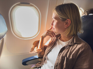 Passenger woman is flying in plane. Girl sitting in airplane looking out window going on trip vacation travel. Traveling female inside plane enjoying flight. Traveling girl