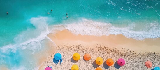 Fototapeta premium Aerial view of a beautiful beach with colorful umbrellas and people swimming in the clear blue water.