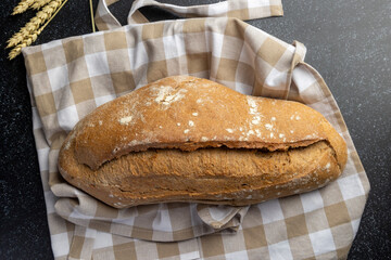 A fresh artisan loaf of bread rests on a crumpled brown paper bag, with wheat stalks nearby, showcasing rustic baking and natural ingredients in a cozy kitchen setting.