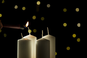 Hand lighting first red candle in the Advent wreath on a festive background with golden...
