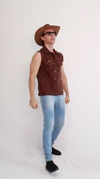 Modelo masculino vaqueiro da moda usando jeans e colete marrom e chap&eacute;u 