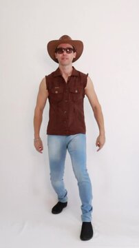 Modelo masculino vaqueiro da moda usando jeans e colete marrom e chap&eacute;u 