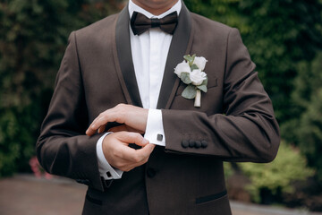 A man with  in a stylish suit  fixes a bow tie. Morning of the groom. Bride helps to fix the groom jacket and accessories