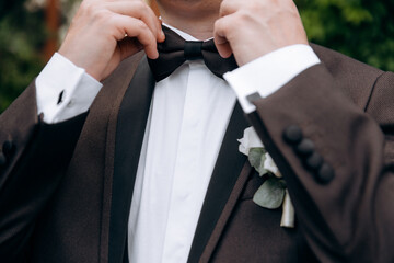 A man with  in a stylish suit  fixes a bow tie. Morning of the groom. Bride helps to fix the groom...