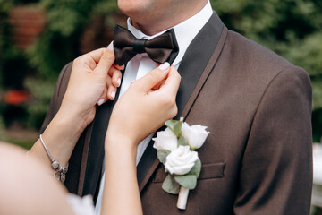 A man with  in a stylish suit  fixes a bow tie. Morning of the groom. Bride helps to fix the groom...