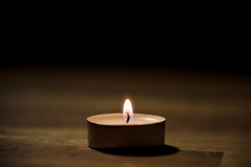 Small white tea candle on a wooden table, close up shot. Tealight ambiance concept.