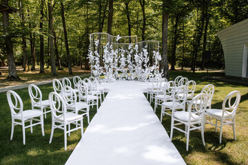 Luxury wedding arch made of white lush flowers on the background of a green forest in summer. Decor for a wedding ceremony