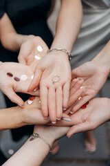 Group photo of a wedding ring in the hands of the bride-to-be on a bachelorette party. Hands of friends girls support the girl