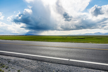 Asphalt road and green grassland nature landscape under blue sky. Road trip.