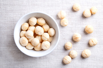 Macadamia nuts, roasted and salted, in a white bowl on linen fabric. Also known as Queensland nut, bush nut, maroochi nut, bauple and Hawaii nuts. Ready-to-eat snack nuts. Close-up, from above. Photo