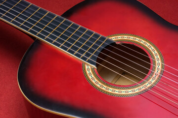 Obraz premium Close-up shot of a red acoustic guitar, focusing on its strings and decorative rosette. The vibrant red color and intricate design add a rich aesthetic appeal to the instrument.