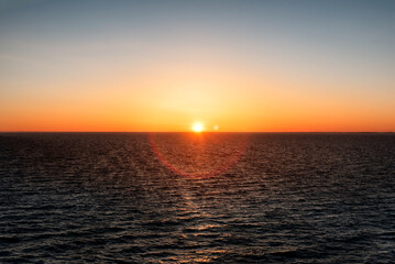 Fototapeta premium Baltic sea at sunset. Clear sky with glowing golden sun, reflections in the water. Setting sun. Epic seascape. Abstract natural pattern, texture, background, concept image