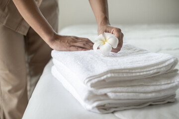Hands of hotel maid putting plumeria flower and towels on the bed in the luxury hotel room ready...