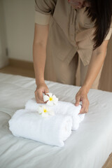 Hands of hotel maid putting plumeria flower and towels on the bed in the luxury hotel room ready for tourist travel