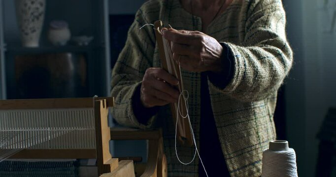 Super slow motion close up of female artisan placing thread before working with woven weaving machine to craft cloth textile piece in her workshop studio at 1000 fps. 