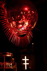A red disco ball with sharp spikes, reflecting light in a retro party setting. The spiked design adds a bold, edgy vibe, creating dynamic reflections and an air of mystery in the dark atmosphere