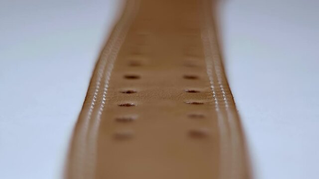 Brown leather belt with double stitching along the edges, even rows of holes. Closeup. Macro. Shallow depth of field. Shot in motion. Follow focus
