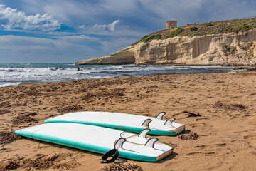 Surfboards on the sandy beach of Santa Caterina di Pittinuri. The watchtower can be seen at the top of the cliff. Sardinia, Italy.