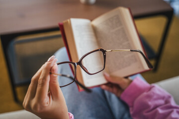 unknown woman sit on sofa read book and hold eyeglasses
