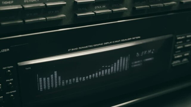 An equalizer with a spectrum analyzer and a compact disc player from which a man's hand extracts a CD, in a hi-fi music center. Closeup. Macro. Shallow depth of field. Shot in motion