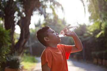 Boy drinking water from a bottle at a public park.