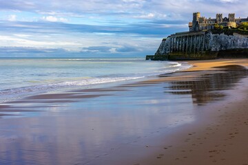 Sandy beach with castle on a cliff under a cloudy sky.