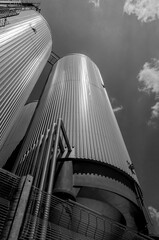 Black and white industrial silos against cloudy sky.