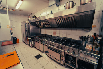 A disorganized restaurant kitchen with visible grime and untidy surfaces. The space appears neglected, with unclean counters and scattered utensils, creating an overall unkempt atmosphere.