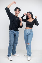 Obraz premium A young asian man and woman in matching black shirts and jeans looking excited raising their hands. Whole body image, against a white background.