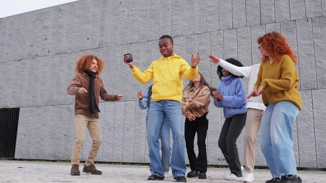 Group of multiethnic friends having fun listening to music from a bluetooth speaker and dancing in the city