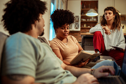 Young friends sitting on couch and reading books at home