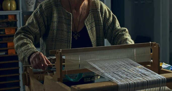 Super slow motion close up of female artisan skillfully working with woven weaving machine, using threads or yarns to craft cloth textile piece in her workshop studio at 1000 fps. 